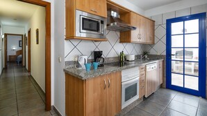 A kitchen with wooden cabinets, a microwave, a stove, and a blue door. - Villa Blanca by Villa Plus (Playa Blanca)