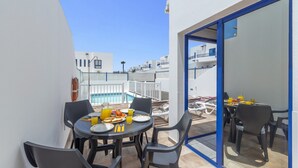 A balcony with a table set for breakfast, overlooking a swimming pool and a white building complex. - Villa Blanca by Villa Plus (Playa Blanca)