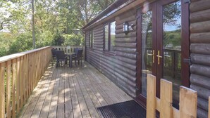 Une terrasse en bois avec une porte vitrée donnant accès à un chalet en rondins.