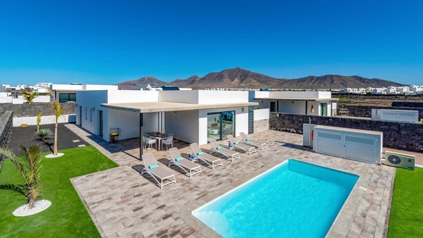 A modern outdoor pool area with lounge chairs, a barbecue, and a view of mountains. - Villa Malvasia by Villa Plus (Playa Blanca)