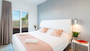 A modern bedroom with a large bed, a sliding glass door to a balcony, and a small bedside table with a plant and a book. - Villa Mifaya by Villa Plus (Playa Blanca)