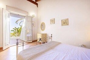 A bedroom with a bed, a dresser, a mirror, and a balcony with a view of palm trees. - Villa Nautilus by Villa Plus (Santa Maria del Focallo)