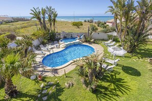 A swimming pool with a curved design, surrounded by lounge chairs and umbrellas, with a view of the ocean in the background. - Villa Nautilus by Villa Plus (Santa Maria del Focallo)