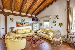 Relax in this inviting living room with a high ceiling, leather sofas, and a wicker rocking chair.