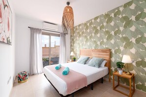 A hotel room with a bed, a window with curtains, an air conditioning unit, a wall with a leaf pattern, and a hanging light fixture.