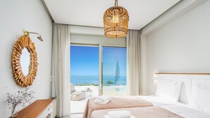 Ein Hotelzimmer mit einem großen Bett, einem Nachttisch aus Holz, einem Spiegel und Blick aufs Meer.