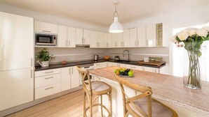 Una cocina moderna con armarios blancos, una isla central con taburetes y un microondas, además de una lámpara colgante.