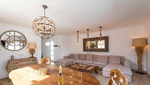 Una sala de estar con una mesa de comedor de madera, un sofá color beige, un espejo redondo y una araña.