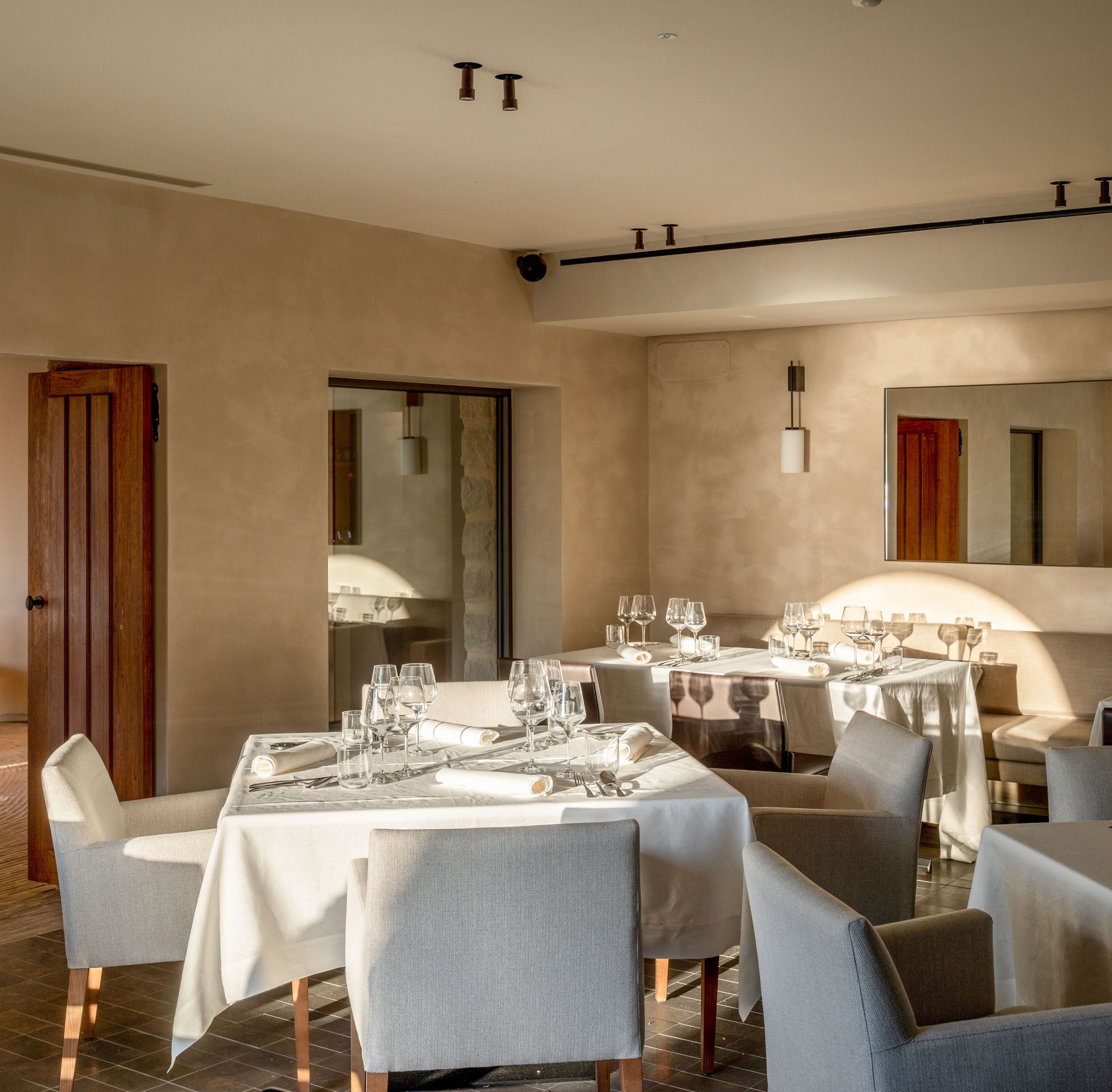 A modern dining area with multiple tables set for a meal, featuring a neutral color palette and contemporary furnishings.