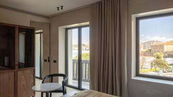 A modern hotel room with a large bed, a small table, a wardrobe, and a balcony with a view of the city.