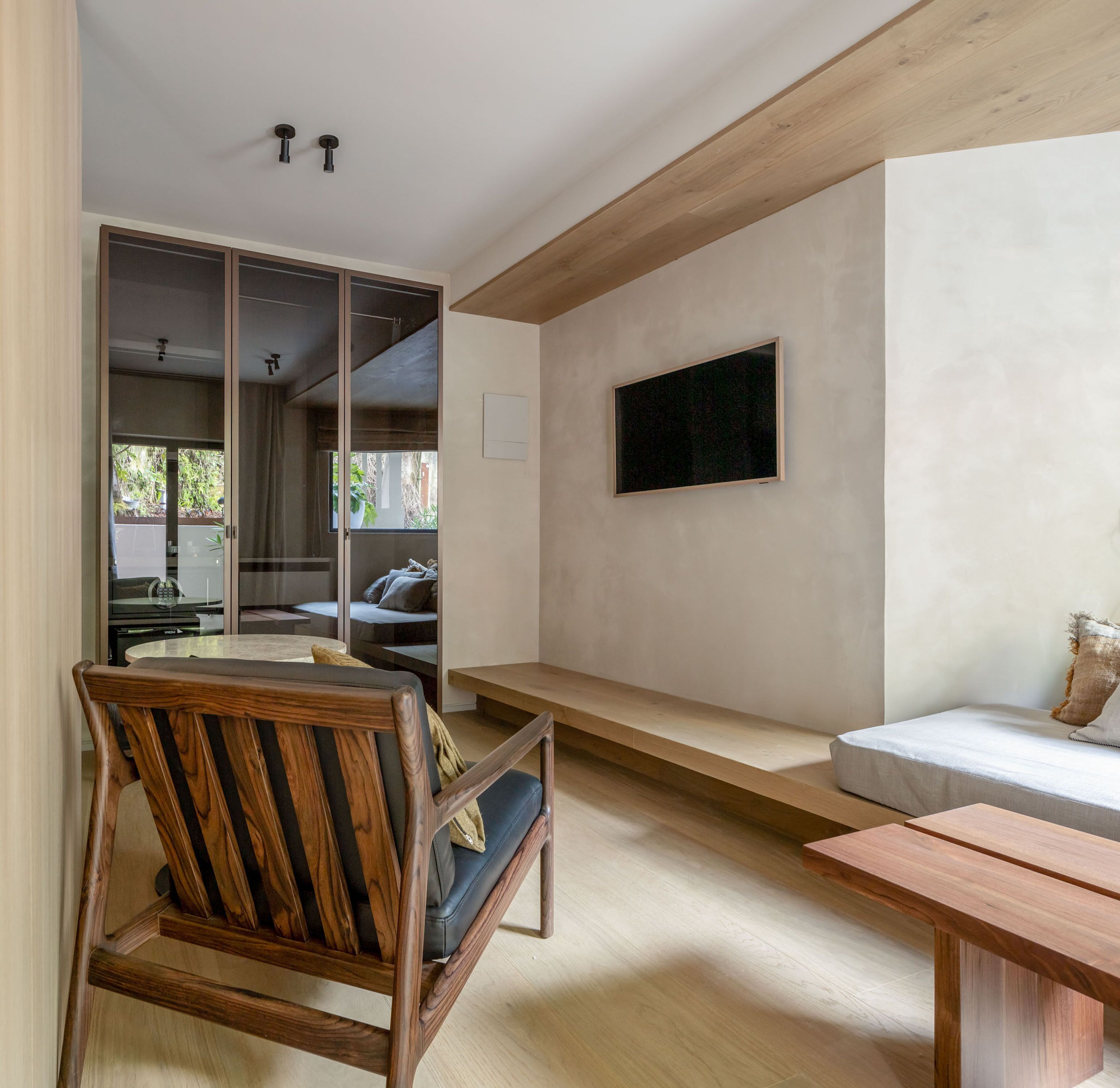 A modern living room with a wooden chair, a bench, and a TV mounted on the wall.