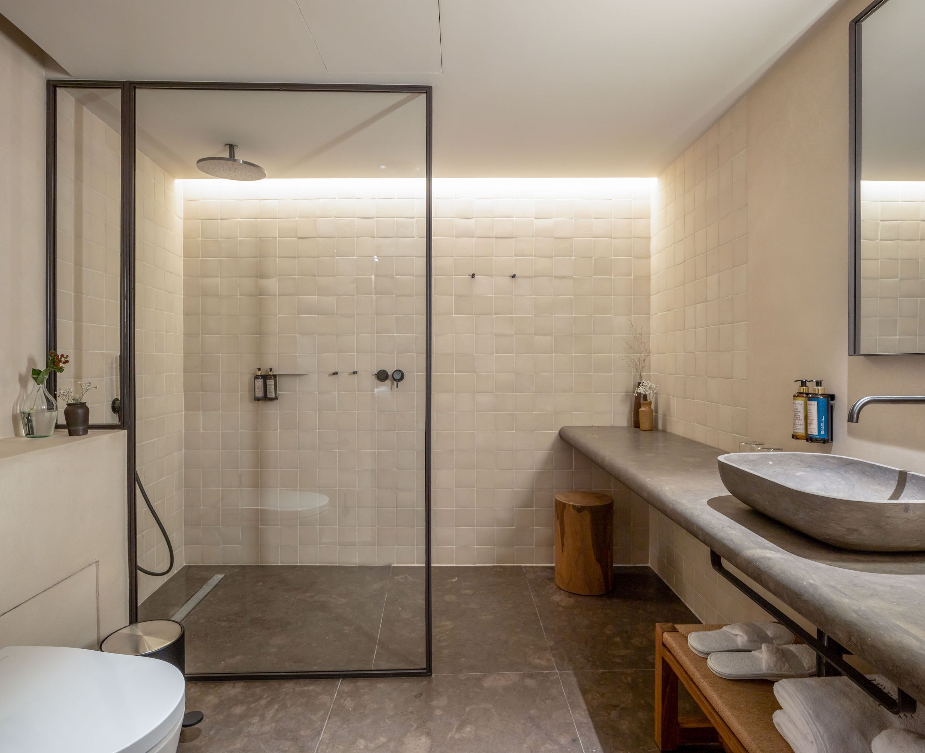 A modern bathroom with a glass-enclosed shower, a round sink, and a wooden bench.