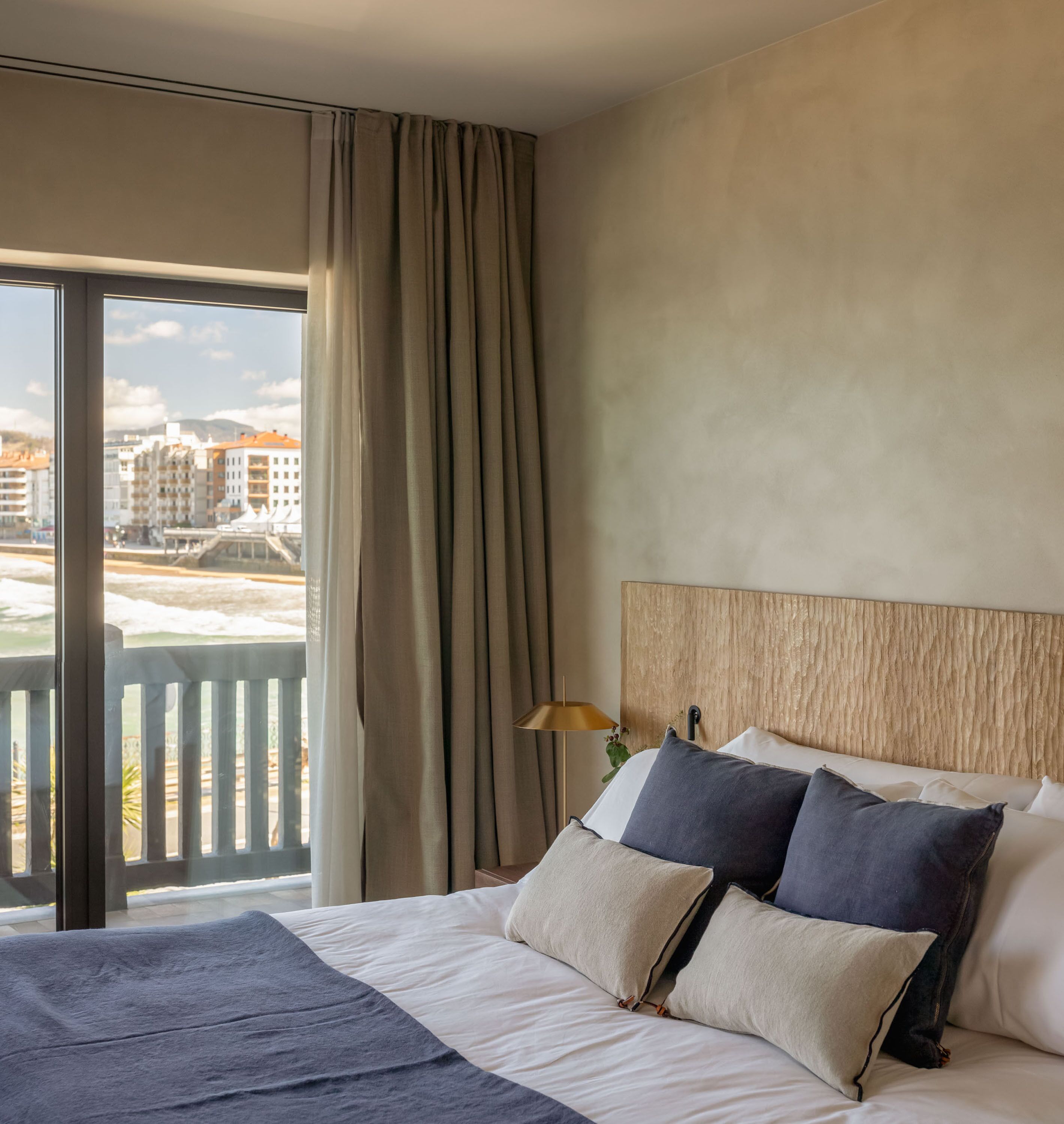 Una habitación de hotel con una cama grande, vistas de edificios a través de una ventana y un balcón.