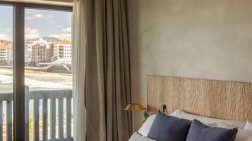Una habitación de hotel con una cama grande, vistas de edificios a través de una ventana y un balcón.