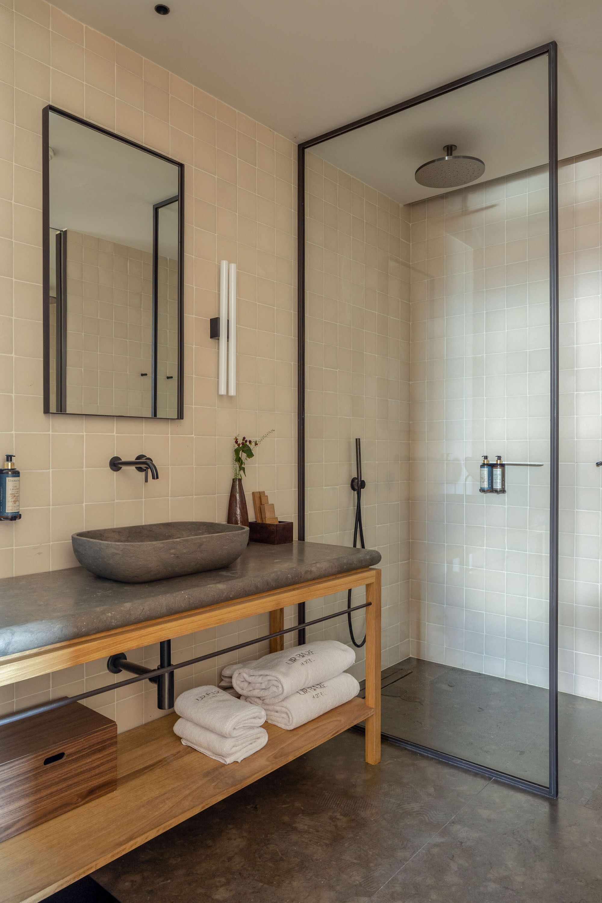 A modern bathroom with a large mirror, a vessel sink, a shower enclosure, and neatly folded towels on a wooden shelf.
