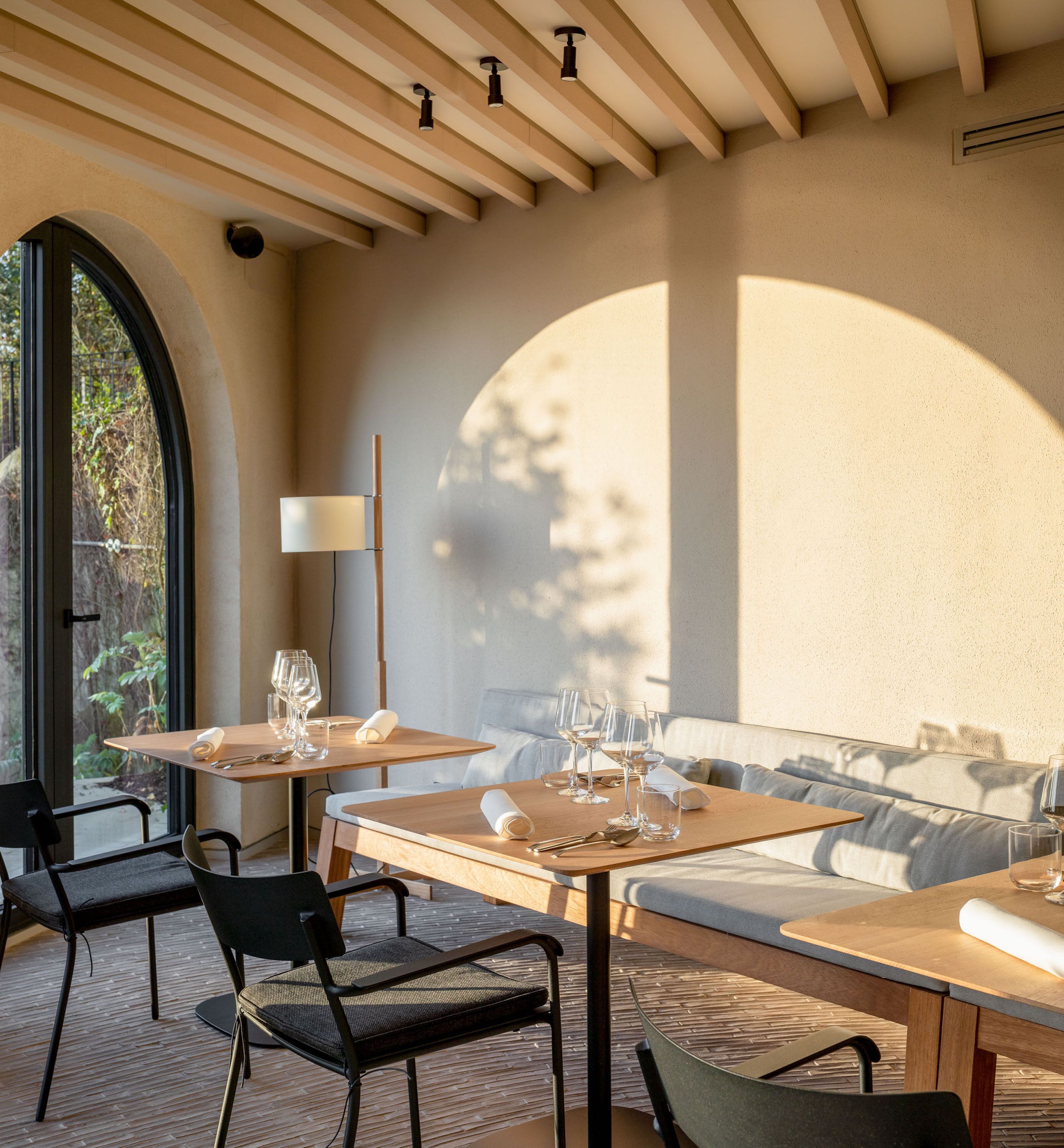 Un espacio moderno para comer al aire libre con mesas y sillas de madera, un sofá y una lámpara.