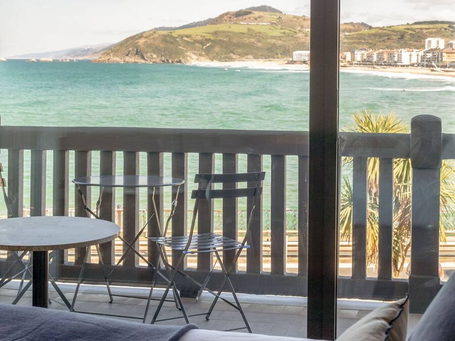 A balcony with a view of the ocean and hills, furnished with a table and chairs.