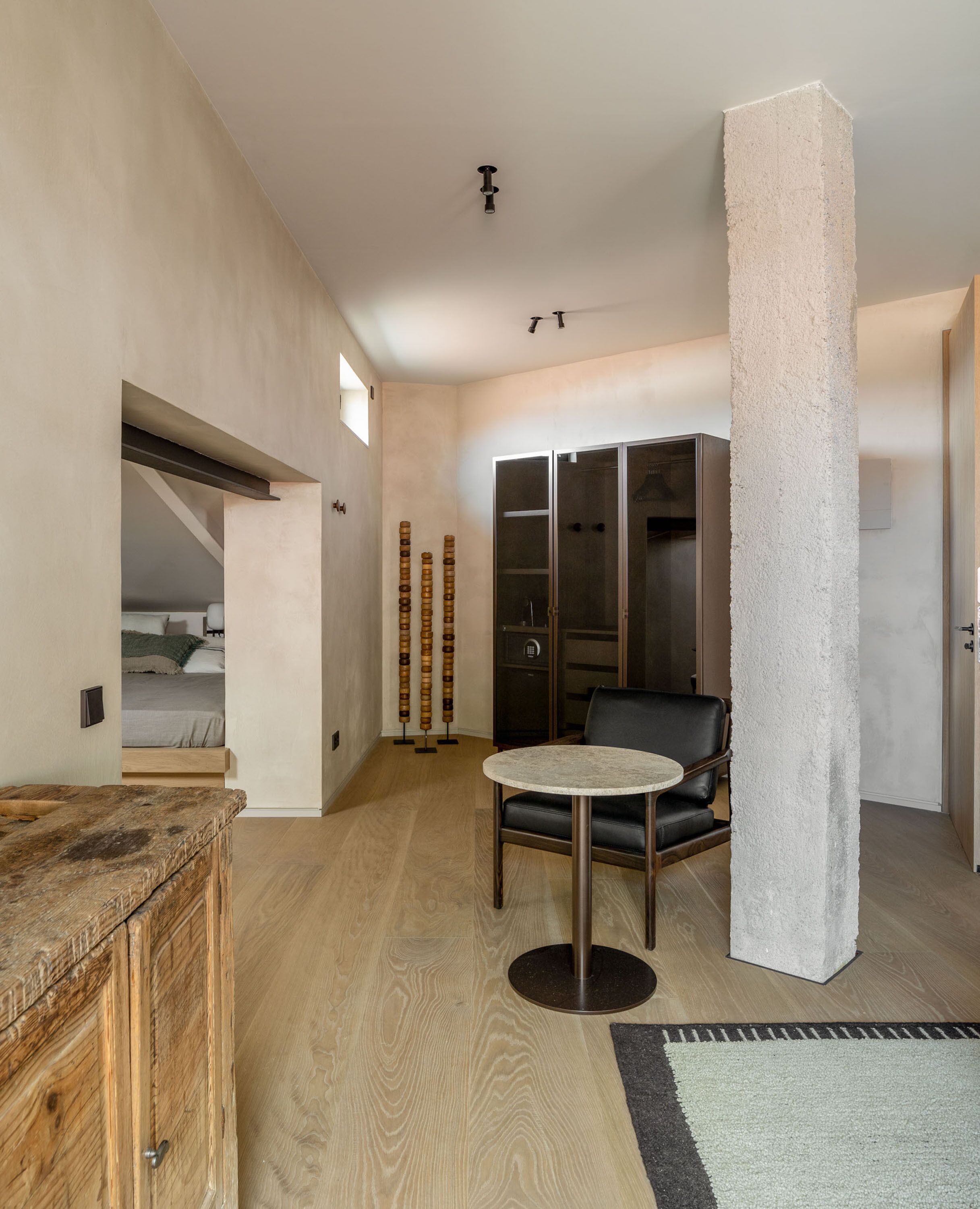 Ein modernes Interieur mit Holzboden, einem runden Tisch, einem schwarzen Ledersessel, einer hohen weißen Säule und einem Kleiderschrank mit Glastüren.