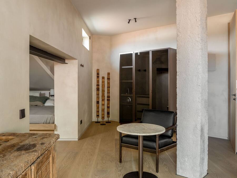 Ein modernes Interieur mit Holzboden, einem runden Tisch, einem schwarzen Ledersessel, einer hohen weißen Säule und einem Kleiderschrank mit Glastüren.
