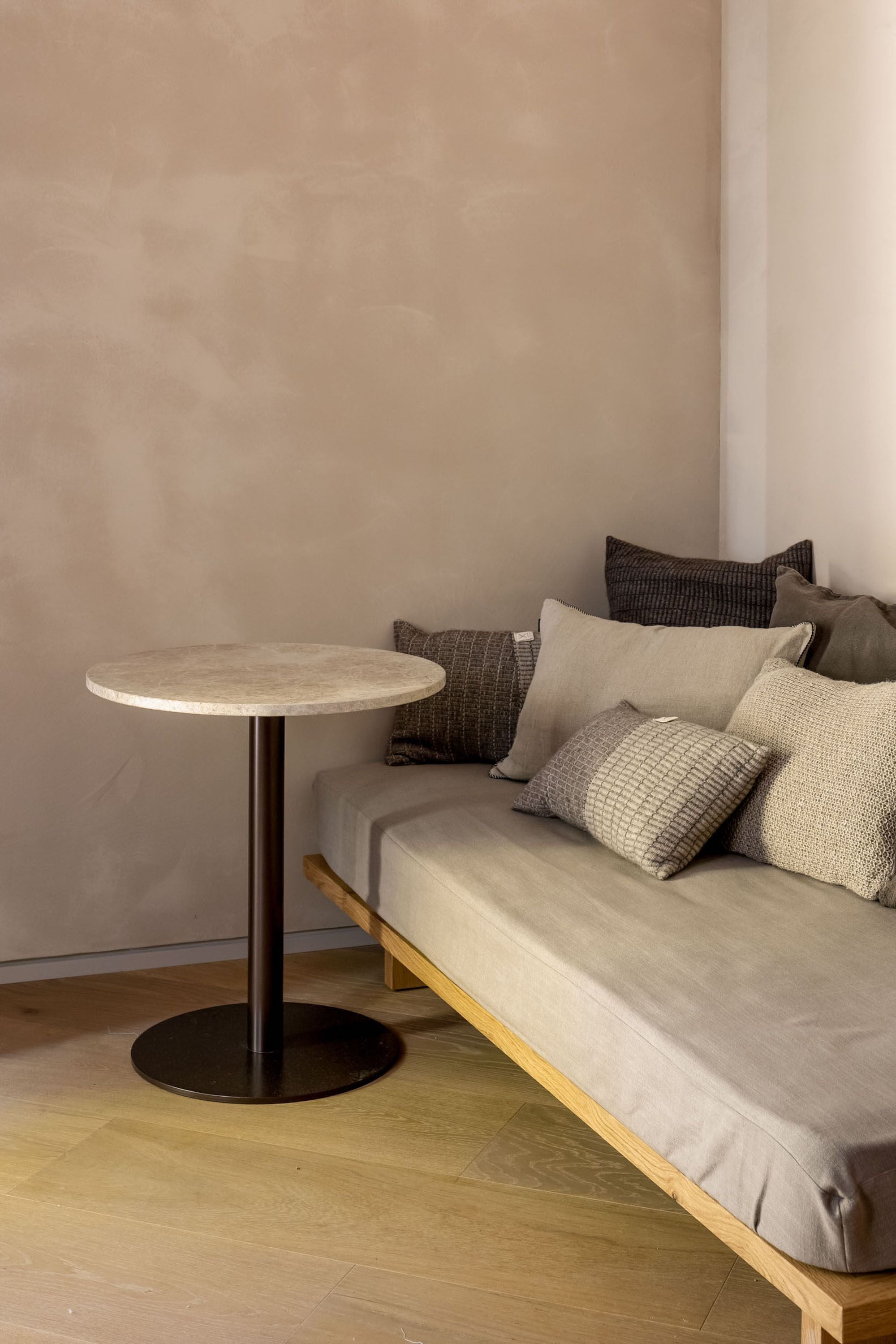A round table with a dark base, positioned next to a sofa with a light-colored cushion.