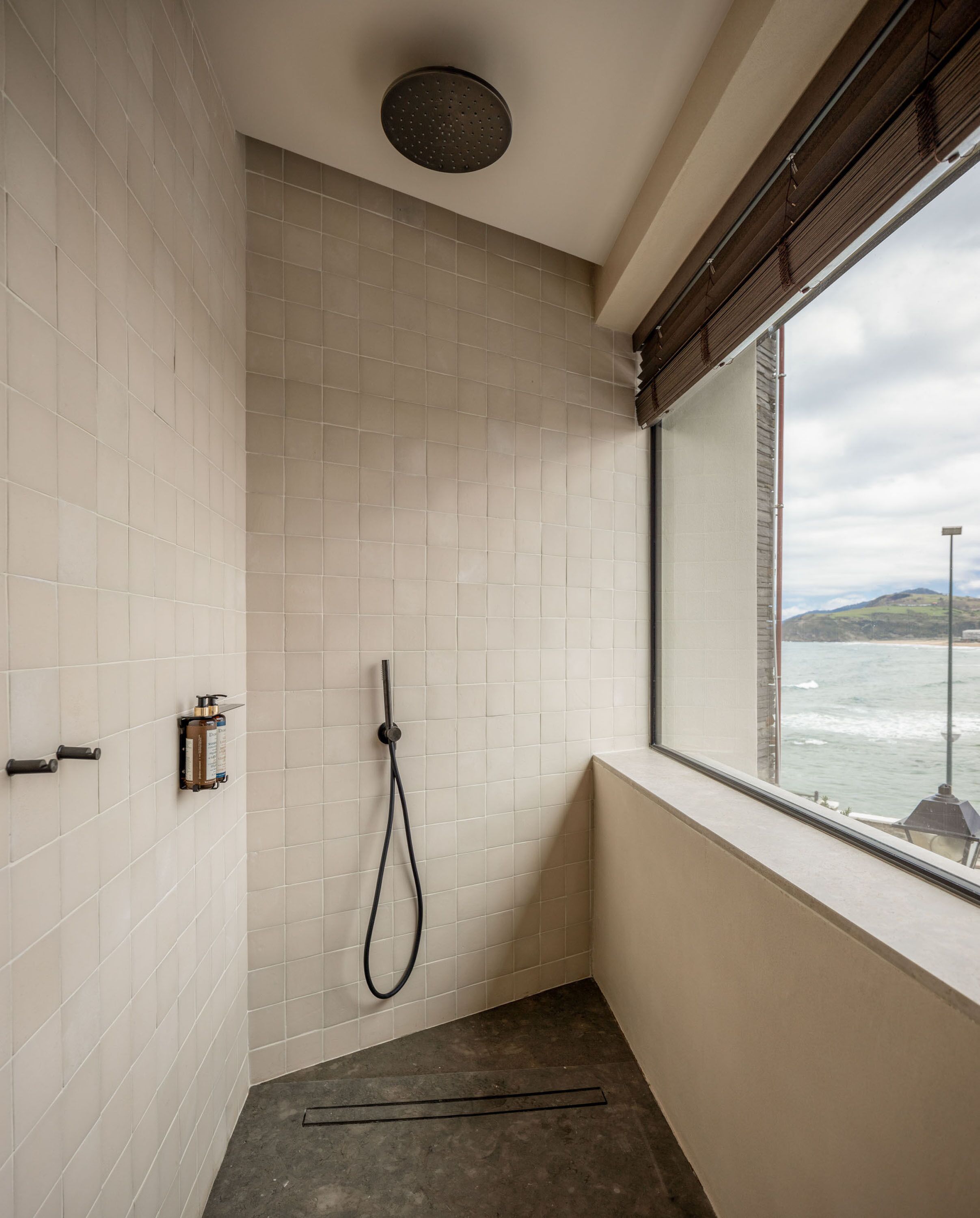 A modern bathroom with a shower, a window with a view of the ocean, and a tiled wall.