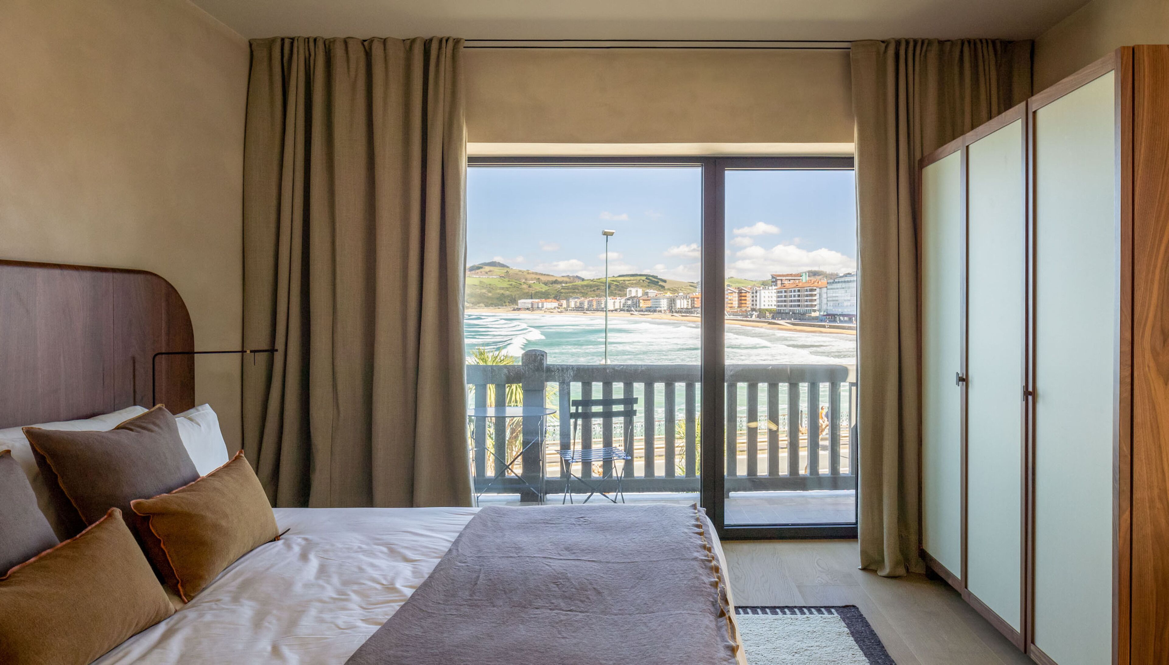 Habitación de hotel con una cama, vista a la playa y balcón con mesa y sillas.