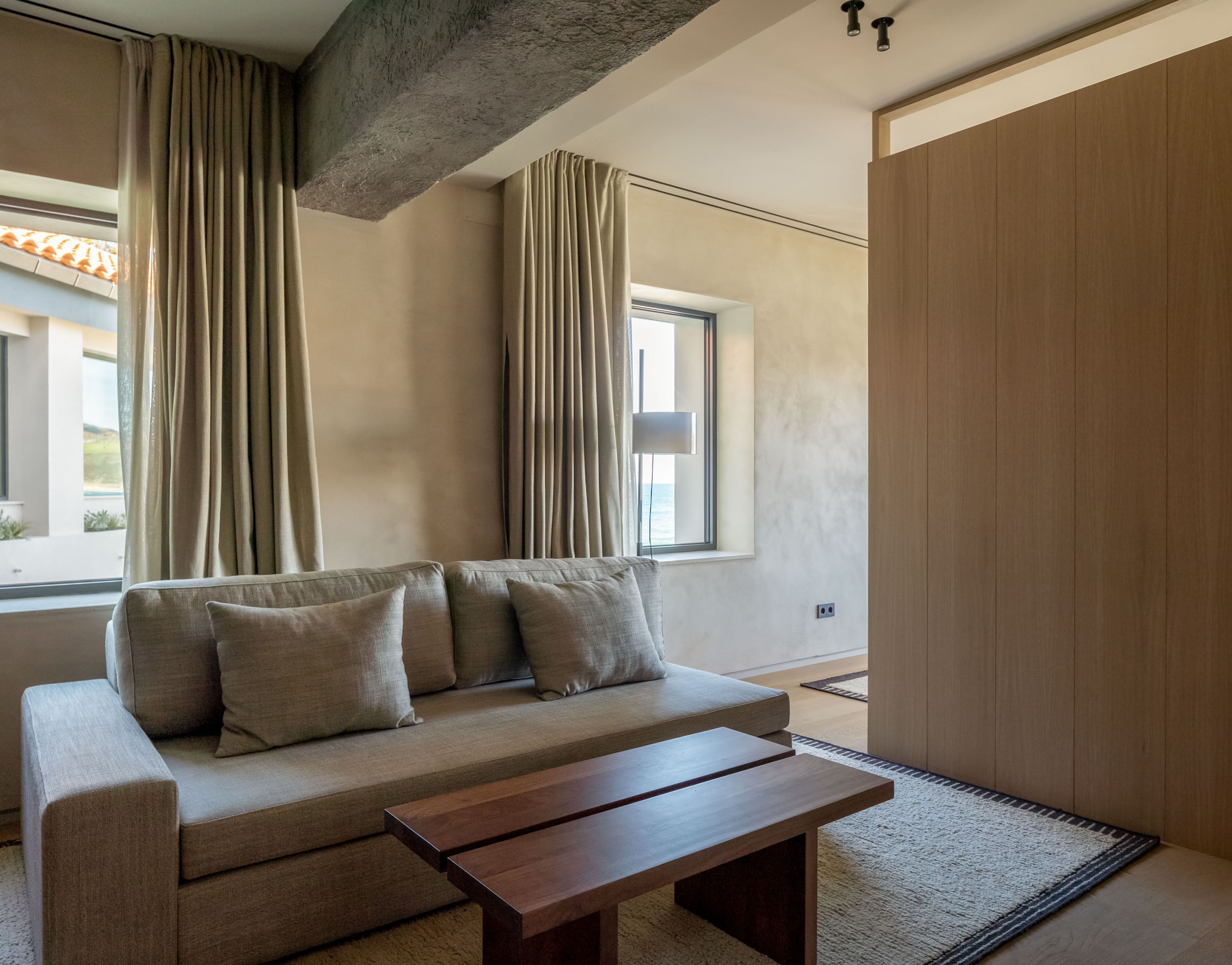 A modern living room with a sofa, a wooden coffee table, and a large window with curtains.