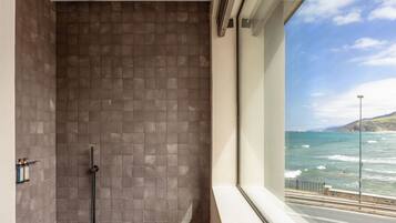 Un baño moderno con ducha, paredes de azulejos y un amplio ventanal con vista al océano.