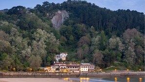 A coastal hotel with multiple buildings, a beach in the foreground, and a forested hill in the background. - Hotel Ur Bare (Zarautz)