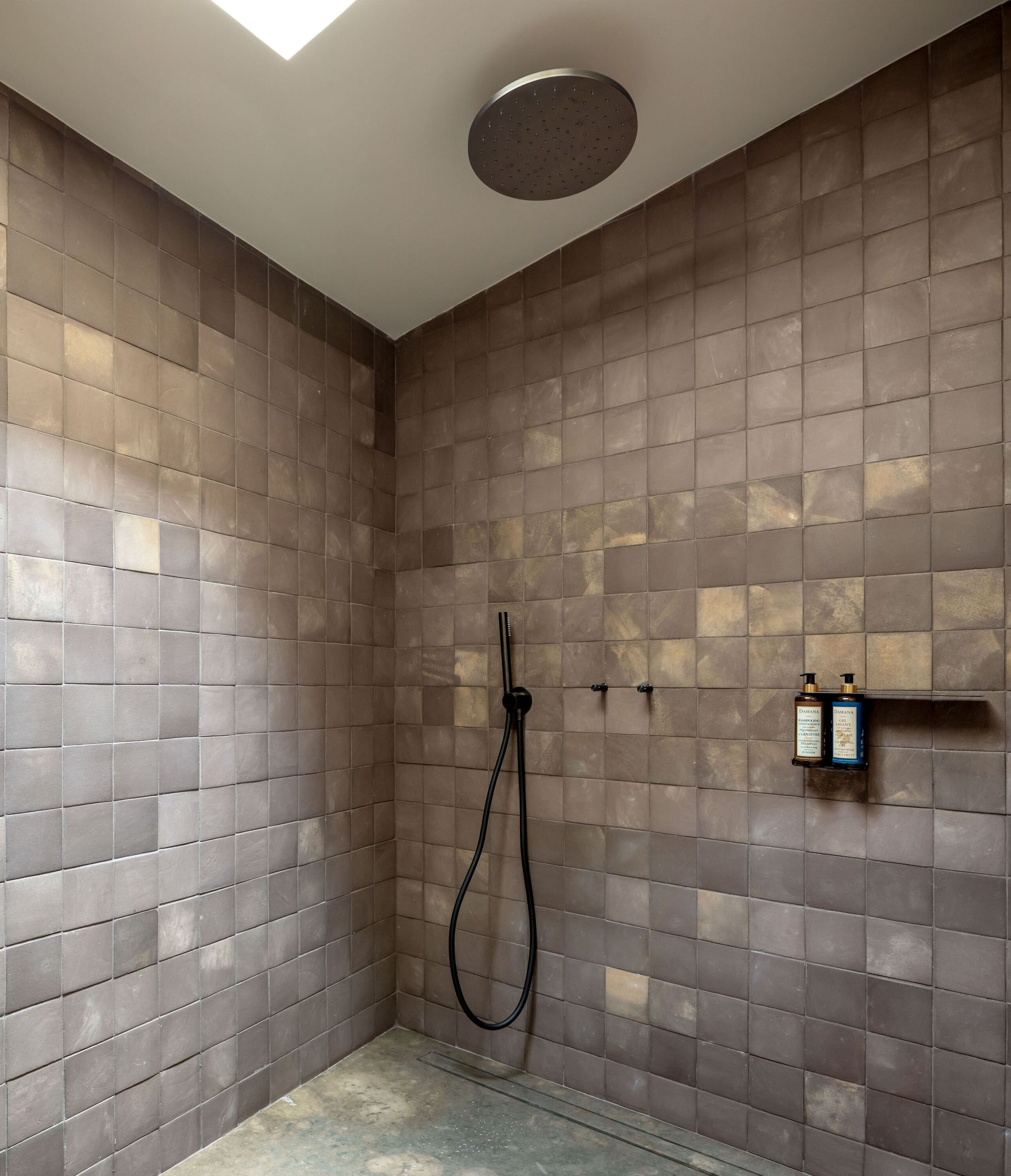 Una ducha con cabezal de ducha manual y grifo de pared. Hay dos botellas de champú y acondicionador en un estante.