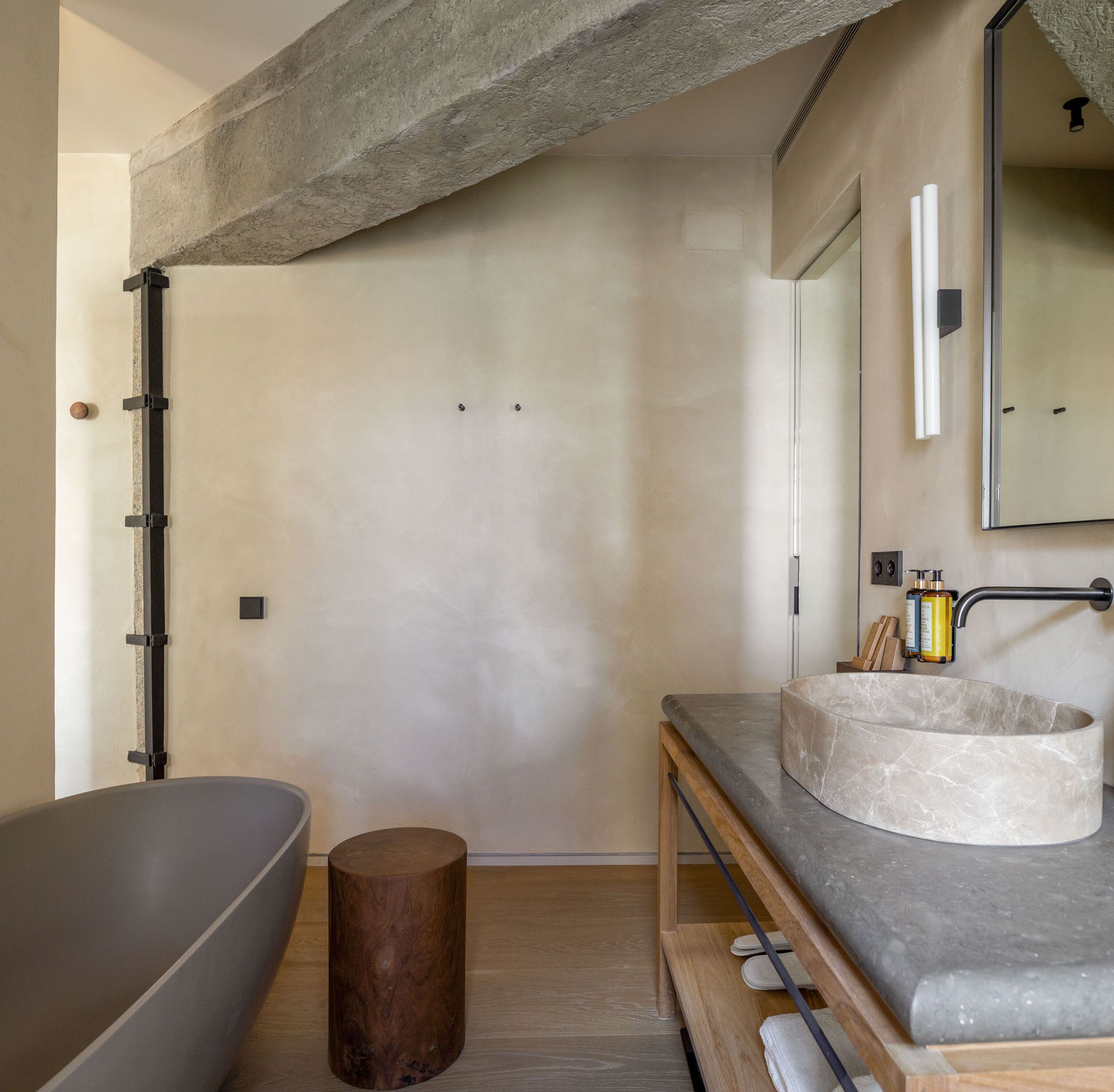 A modern bathroom with a freestanding bathtub, a round marble sink, and a wooden stool.