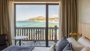 A hotel room with a bed, a small table, and a chair, a balcony with a view of the ocean and a hilly landscape. - Hotel Ur Bare (Zarautz)