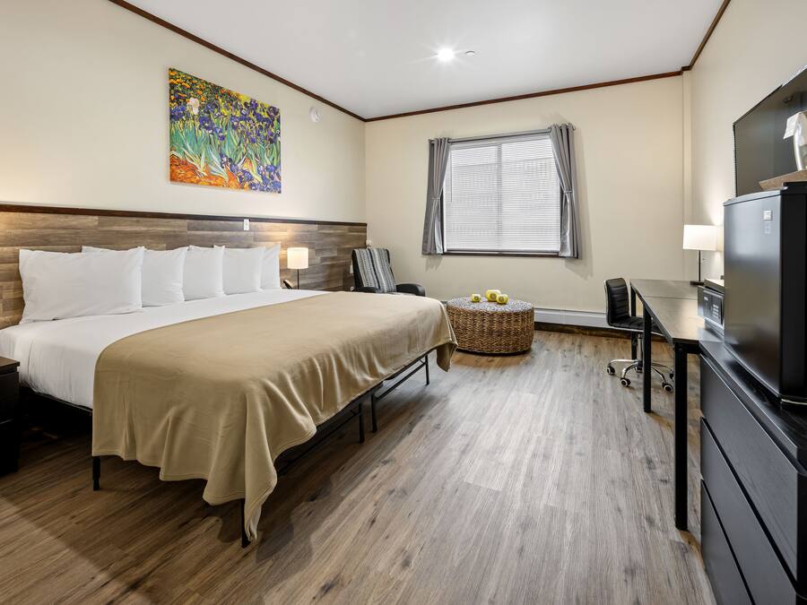 A hotel room with a bed, a desk, a television, and a painting on the wall.
