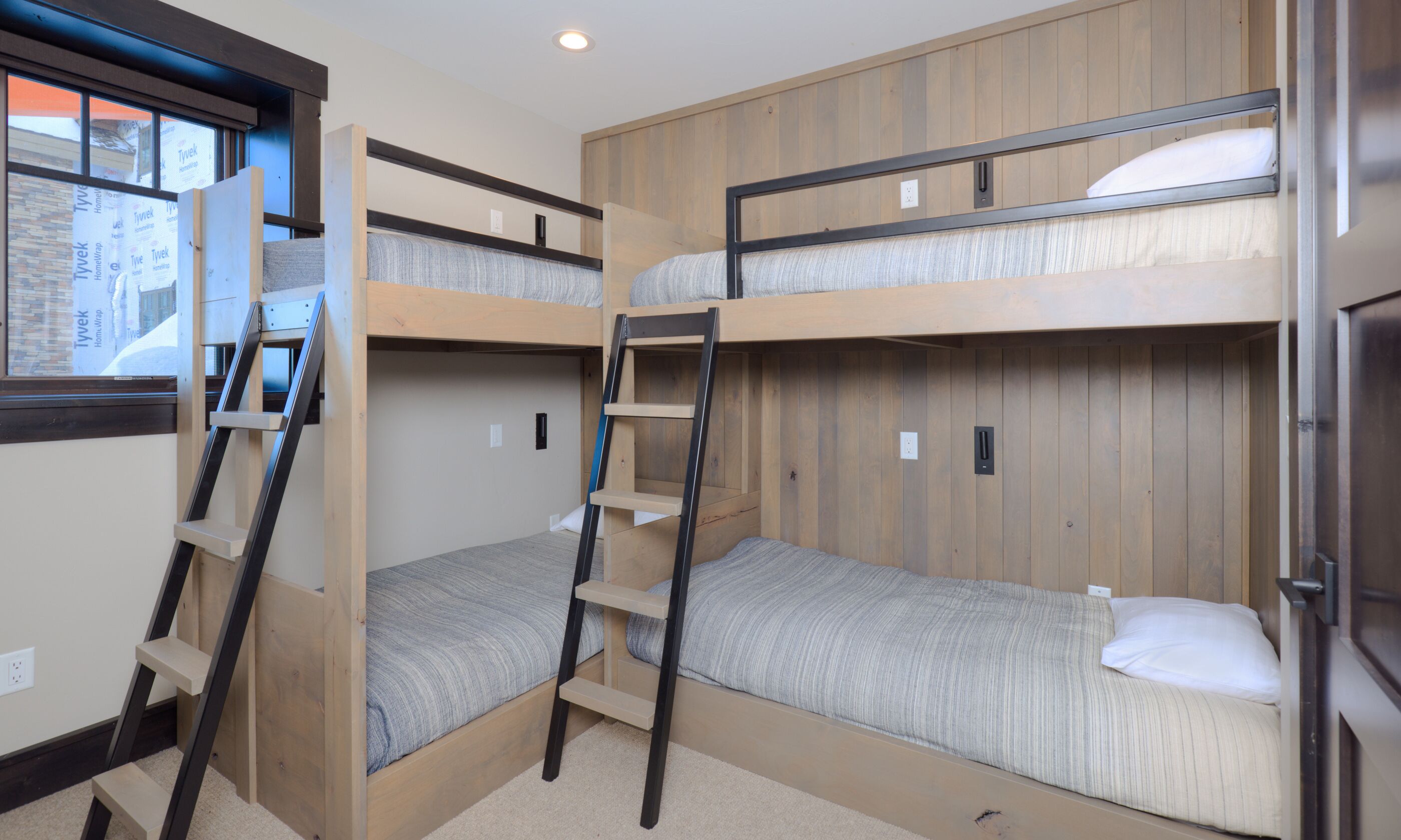 A bunk bed room with a ladder, wooden walls, and a window.