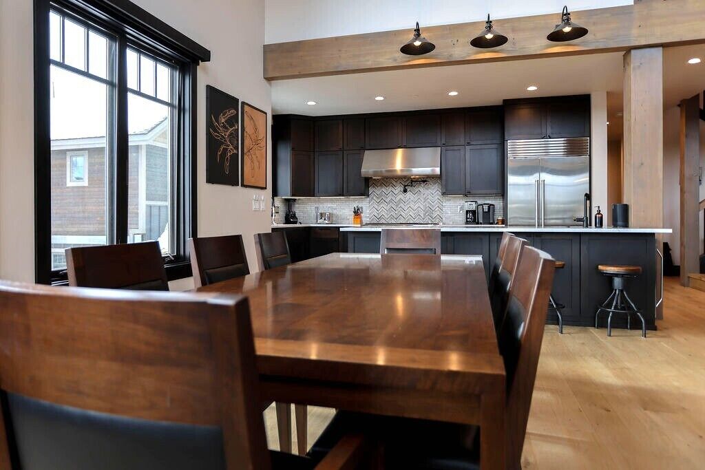 A modern kitchen with dark cabinets, stainless steel appliances, and a large dining table.