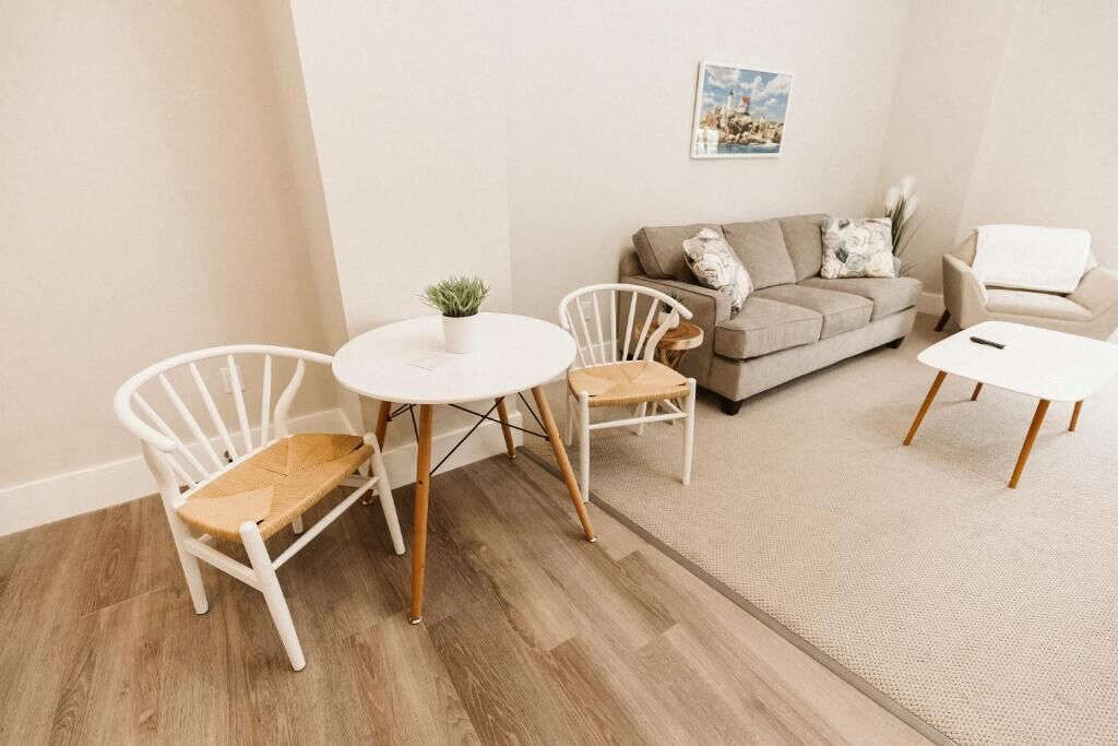 Una sala de estar con un sofá color beige, dos sillas blancas, una mesita redonda y un centro de café.