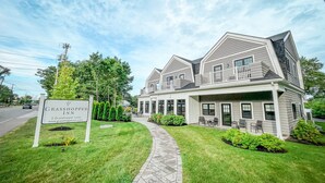 A two-story building with a sign for Grasshopper Inn, featuring a covered patio area with outdoor seating. - Grasshopper Inn (Ogunquit)