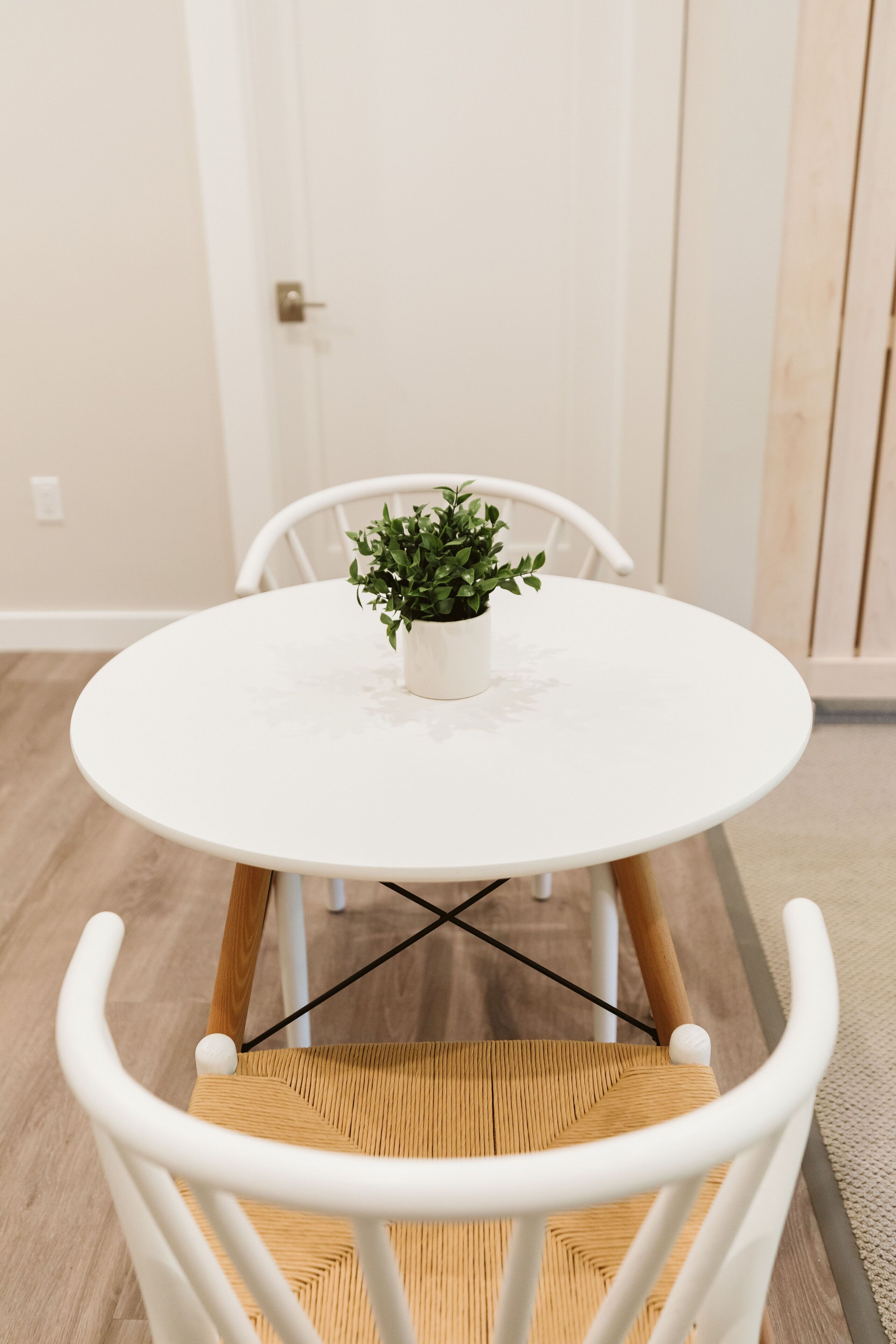 Ein runder weißer Tisch mit einem Blumentopf, umgeben von weißen Stühlen mit Holzbeinen und gewobenen Sitzflächen.