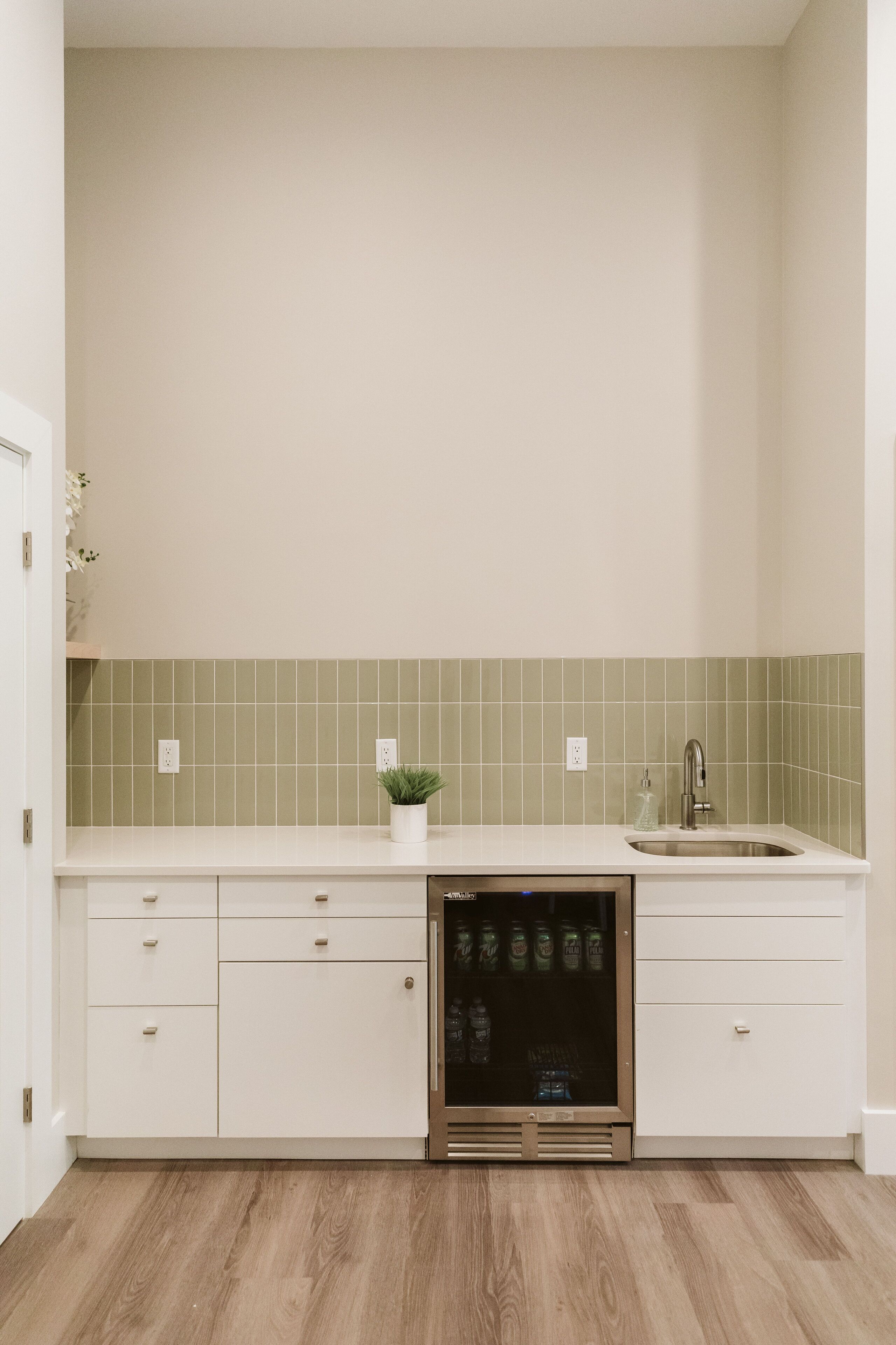 A kitchen with white cabinets, a green tiled backsplash, a built-in dishwasher, and a sink.