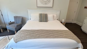A neatly arranged bedroom with a large bed, a chair, a wall-mounted artwork, and a door.