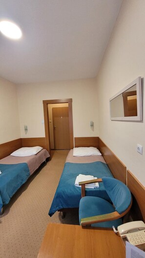 A hotel room with two single beds, a wooden nightstand, a desk with a telephone, and a mirror on the wall. - Geovita Dabki (Darlowo)