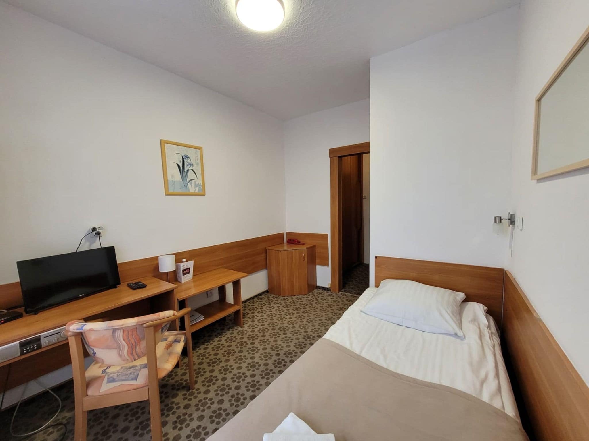 A hotel room with a bed, desk, chair, TV, and a small table.