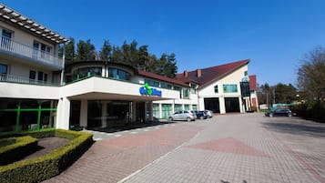 A building with a 'Coca-Cola' sign, a covered entrance, and a parking area with cars.