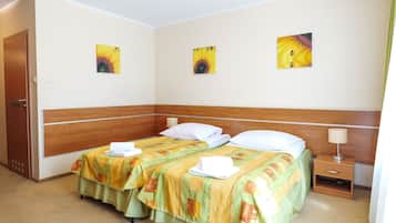 A hotel room with two beds, a wooden headboard, a nightstand with a lamp, and three wall-mounted paintings.