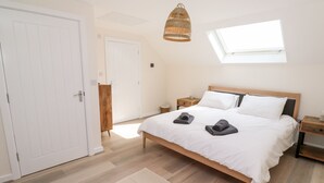 A bedroom with a bed, a wooden wardrobe, a nightstand, a hanging light fixture, and a skylight. - The Bright House (Wadebridge)
