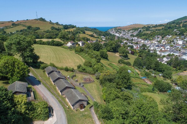 Un paysage rural avec un petit groupe de maisons traditionnelles, une route sinueuse et une vue lointaine d’une agglomération plus importante.