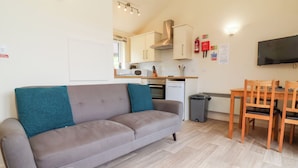 A compact living space with a sofa, a dining table with chairs, a kitchenette, and a TV mounted on the wall. - 11 Manleigh Park (Ilfracombe)
