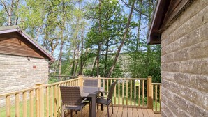 Une terrasse en bois avec une table et des chaises, entourée d’une clôture en bois et d’un bâtiment en pierre.
