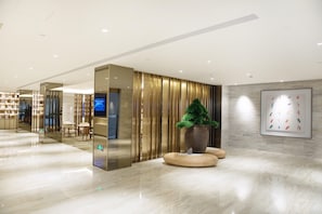 A modern lobby with a polished marble floor, a reception desk, a large potted plant, and a framed artwork on the wall. - Ji Hotel Shanghai New Jiangwan City Yingao Road (Shanghai)