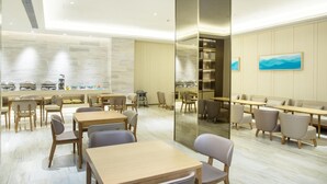 A modern dining area with wooden tables and chairs, a central column, and a view of the kitchen through a glass partition. - Ji Hotel Shanghai New Jiangwan City Yingao Road (Shanghai)